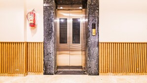 Un ascensor con marco de mármol, un extintor en la pared y diseño de paneles de madera en el suelo.