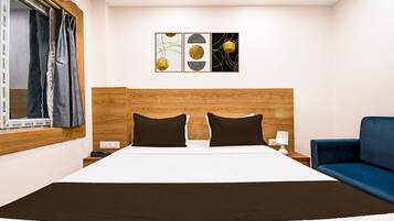 A hotel room with a bed, two nightstands, a blue armchair, and three wall art pieces.