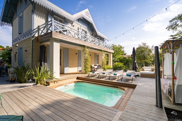 A poolside area with a wooden deck, lounge chairs, and a small pool.