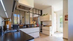 Une cuisine moderne dotée d’un grand îlot central, d’appareils électroménagers intégrés et offrant une vue sur l’extérieur.