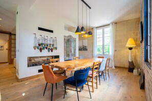 A dining area with a wooden table, blue and orange chairs, hanging pendant lights, and a fireplace.