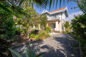 A traditional house with a tiled roof, surrounded by lush greenery and a paved driveway.