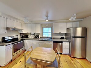Una cocina moderna con armarios blancos, electrodomésticos de acero inoxidable, una mesa de comedor de madera y una ventana que proporciona luz natural.