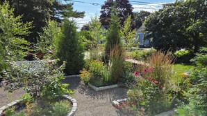 Ein Garten mit Kieswegen, verschiedenen Pflanzen und einem weißen Zaun.