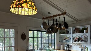 Ett kök med en hängande hylla för kastruller, en köksö i trä och en lampa med färgat glas.