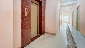 A hallway with a red-tiled wall, a door with a handle, and a patterned floor. - Super Hotel O Anna Nagar Madurai (Madurai)