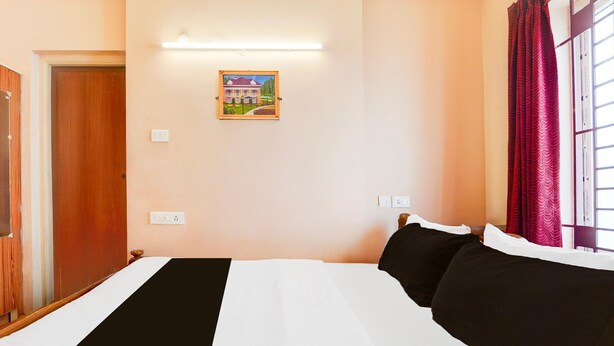 A hotel room with a bed, a door, a wall-mounted light, and a window with curtains. - Super Hotel O Anna Nagar Madurai (Madurai)