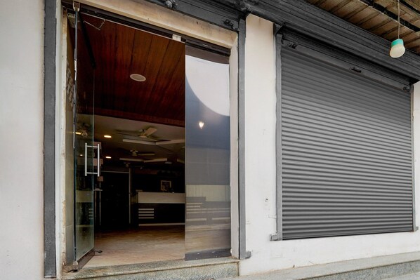 A building entrance with a glass door, a closed roller shutter, and a ceiling fan.