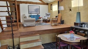Een ruime woonkamer met een trap, een eettafel met stoelen, een bank en een blauwe kast.