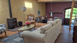 Een gezellige woonkamer met een bank, een tafel met bloemen, een open haard en een keuken in de achtergrond.