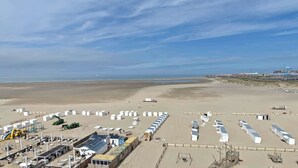 A beachside facility with rows of white tents, a sandy beach, and industrial structures in the background. - Beachfront Loft Terrace & Sea View in Zeebrugge (Brugge)