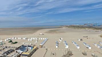 Un complexe situé en bord de mer, avec des rangées de tentes blanches, une plage de sable et, en arrière-plan, des bâtiments industriels.