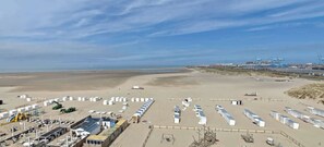 A beachside facility with rows of white tents, a sandy beach, and industrial structures in the background. - Beachfront Loft Terrace & Sea View in Zeebrugge (Brugge)