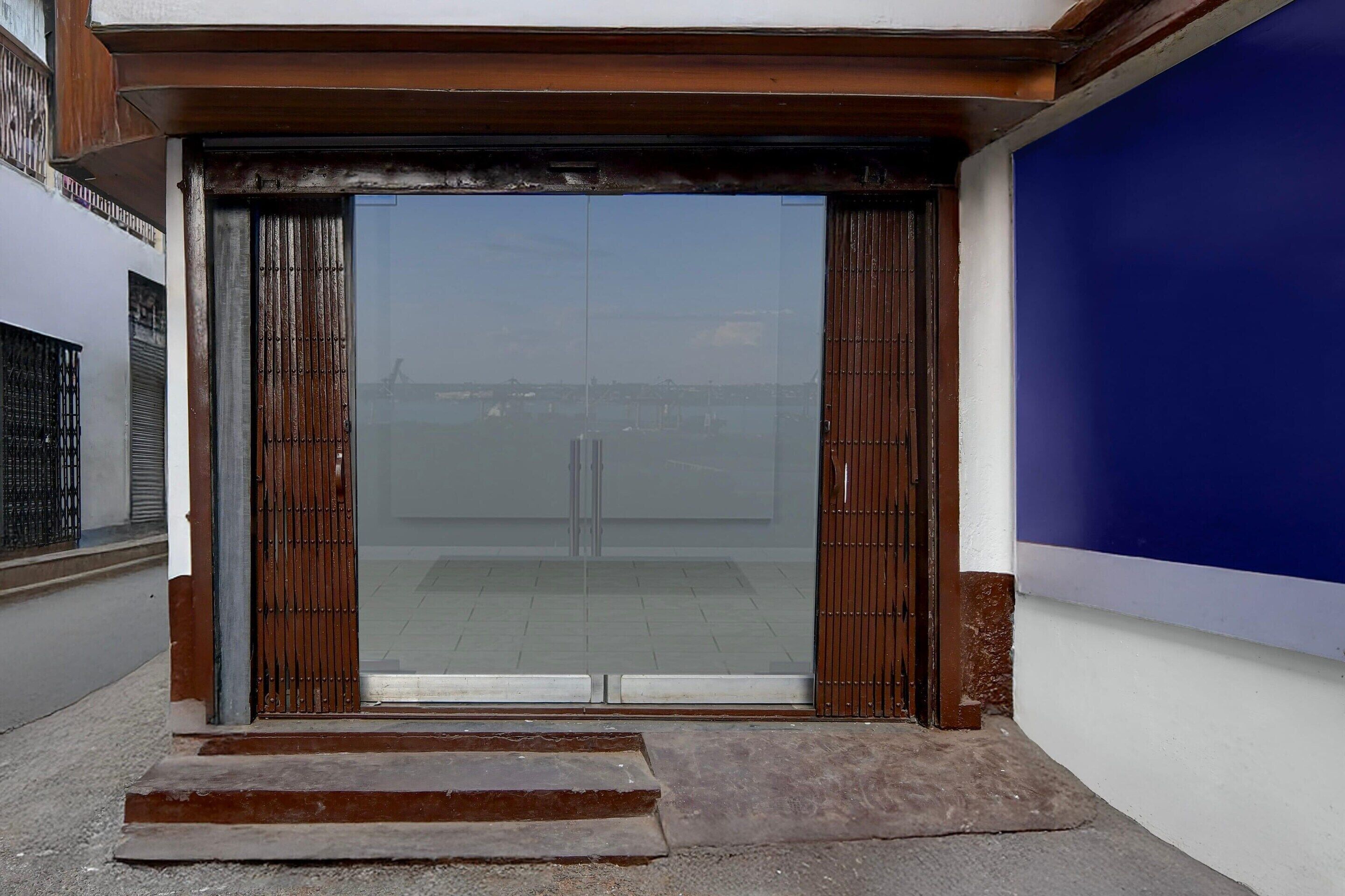 A building entrance with a large glass door, steps leading up to it, and a blue wall to the right.