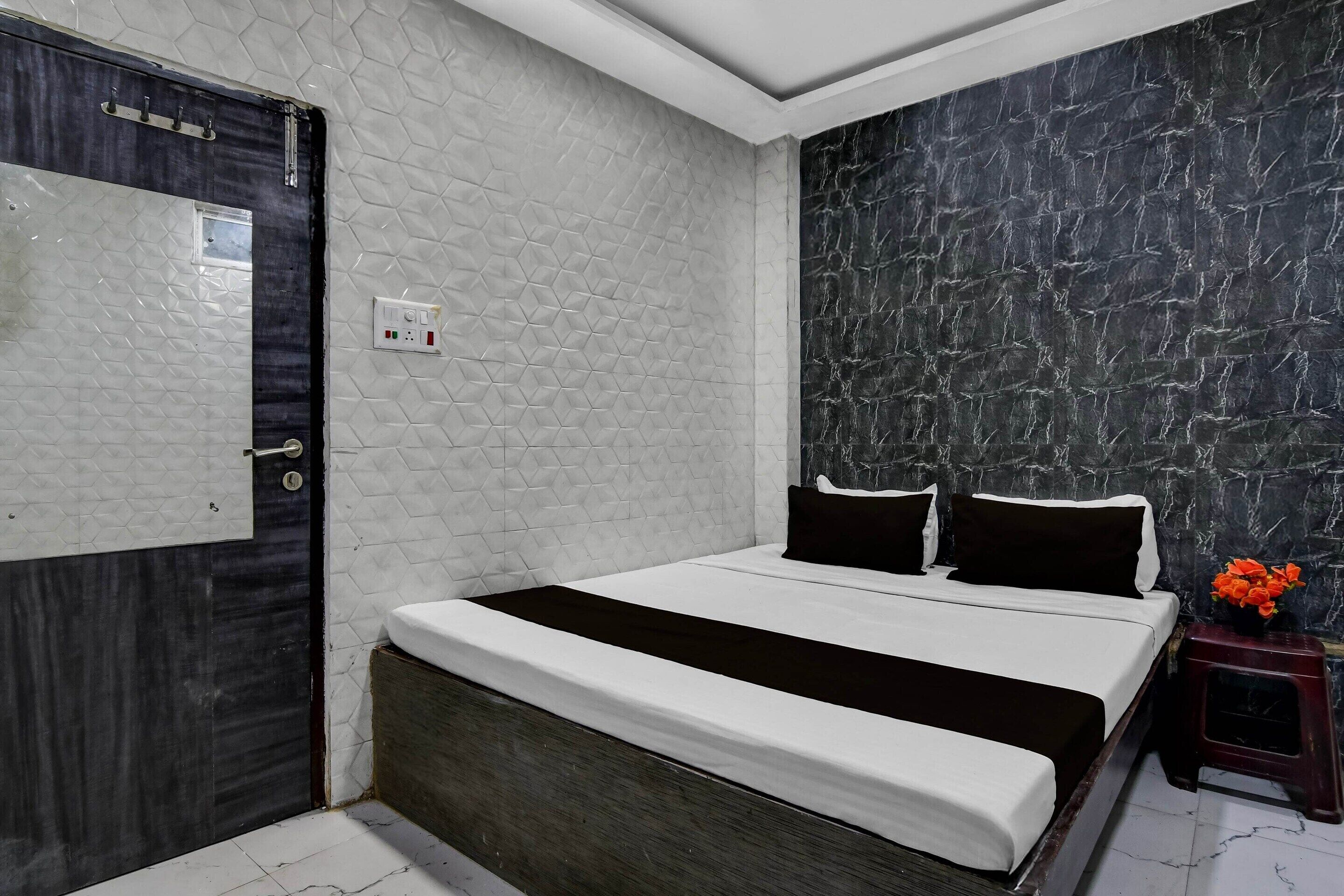 Quarto com cama, mesa de cabeceira, luminária na parede e porta.