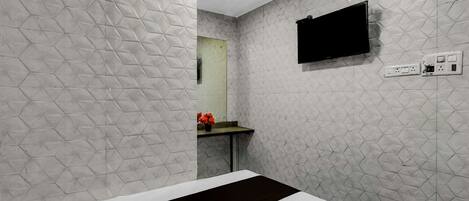 A hotel room with a bed, a flat-screen TV mounted on the wall, a small table with a vase of flowers, and a mirror.