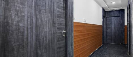 A hallway with dark wooden doors, a wooden panel wall, and a tiled floor.