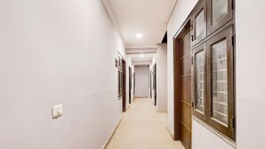 A narrow hallway with white walls, a light-colored floor, and wooden doors with glass panels. - Saver Single Hotel Chhillar Inn (New Delhi)