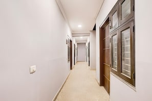 A narrow hallway with white walls, a light-colored floor, and wooden doors with glass panels. - Saver Single Hotel Chhillar Inn (New Delhi)