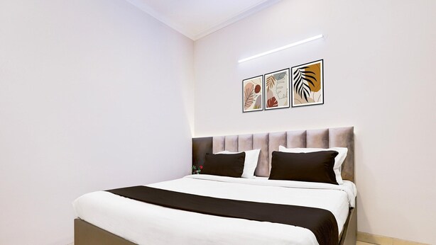 A neatly made bed with a headboard, white and black bedding, and two wall-mounted artworks. - Saver Single Hotel Chhillar Inn (New Delhi)