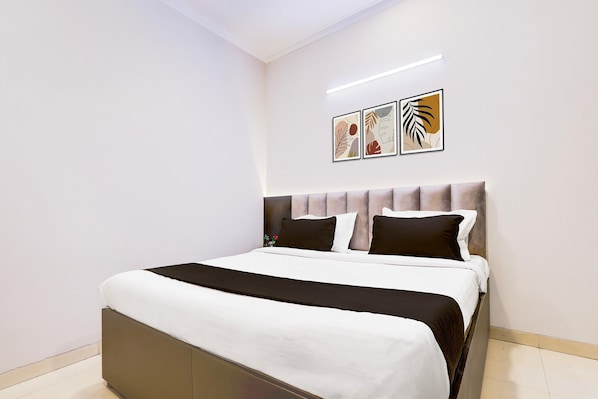 A neatly made bed with a headboard, white and black bedding, and two wall-mounted artworks. - Saver Single Hotel Chhillar Inn (New Delhi)