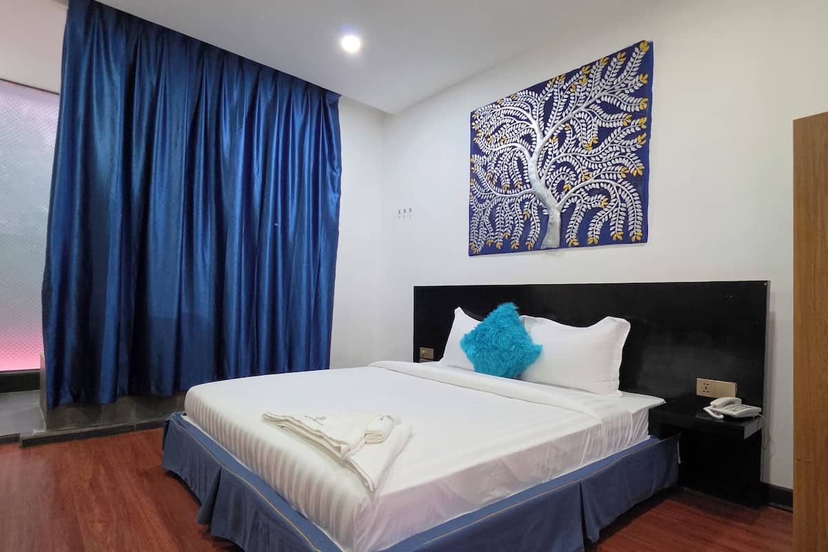 Une chambre d’hôtel comprenant un lit, une table de chevet, un téléphone, un tableau décoratif et une fenêtre avec des rideaux.