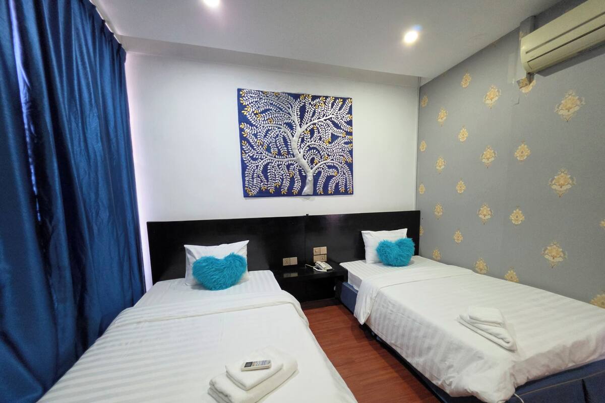 Une chambre d’hôtel avec deux lits, un rideau bleu, une œuvre d’art murale et un papier peint à motifs.