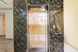 An elevator with a metallic finish, set in a hallway with a marble wall featuring gold streaks.
