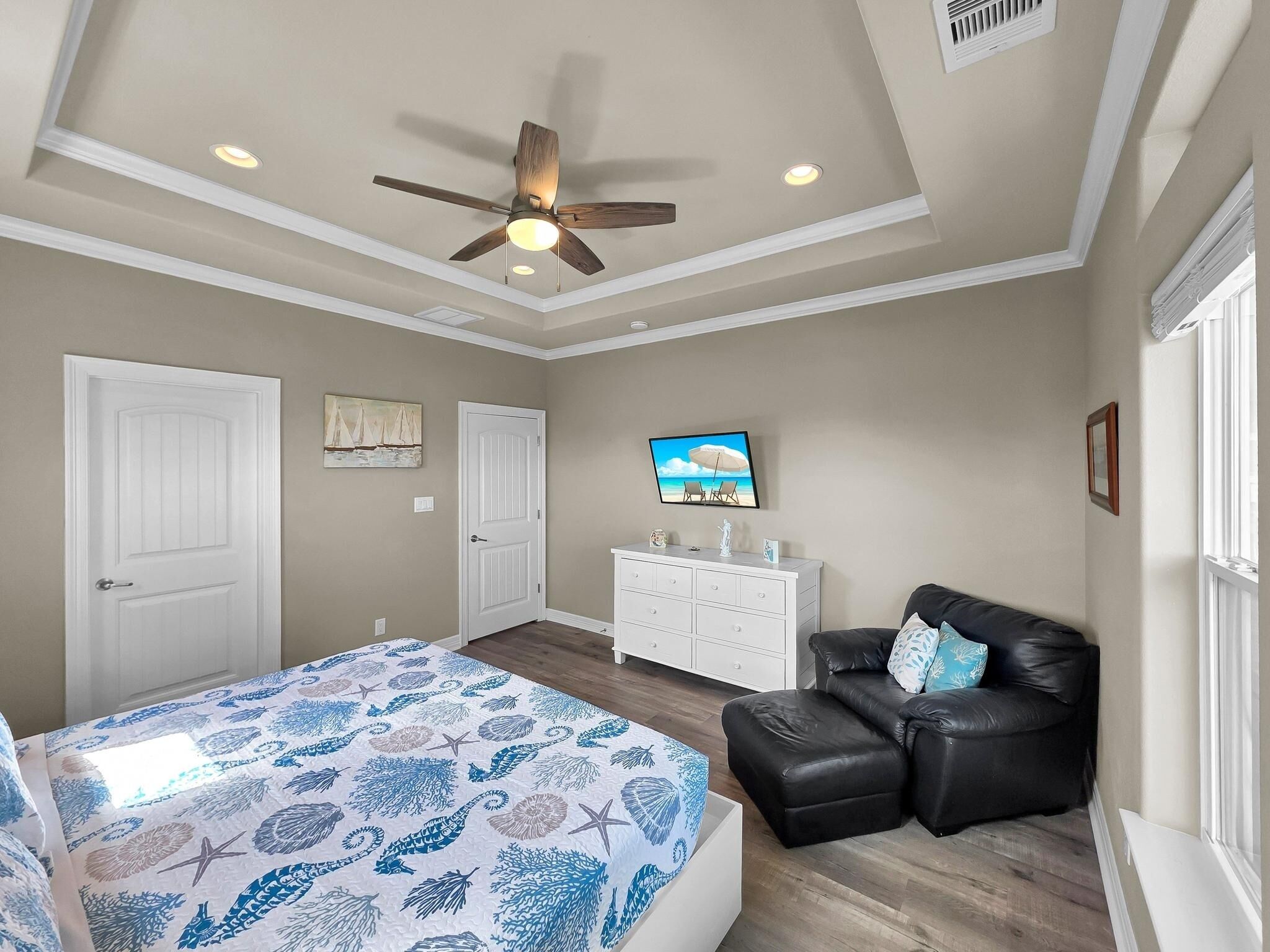 Un dormitorio con cama, ventilador de techo, cómoda, televisor y ventana.