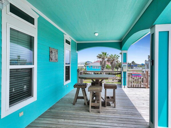 A covered porch with a table and chairs, a blue building in the background, and a 'Keep Gate Closed' sign. - Heaven's Song 3 Bedroom Home (Port Bolivar)
