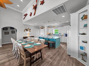 A spacious kitchen with white cabinets, a central island, and a dining area with wooden chairs and a table set for four. - Heaven's Song 3 Bedroom Home (Port Bolivar)