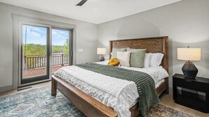Ein Schlafzimmer mit einem großen Bett, einem Deckenventilator, einem Nachttisch und Blick durch eine Glasschiebetür.
