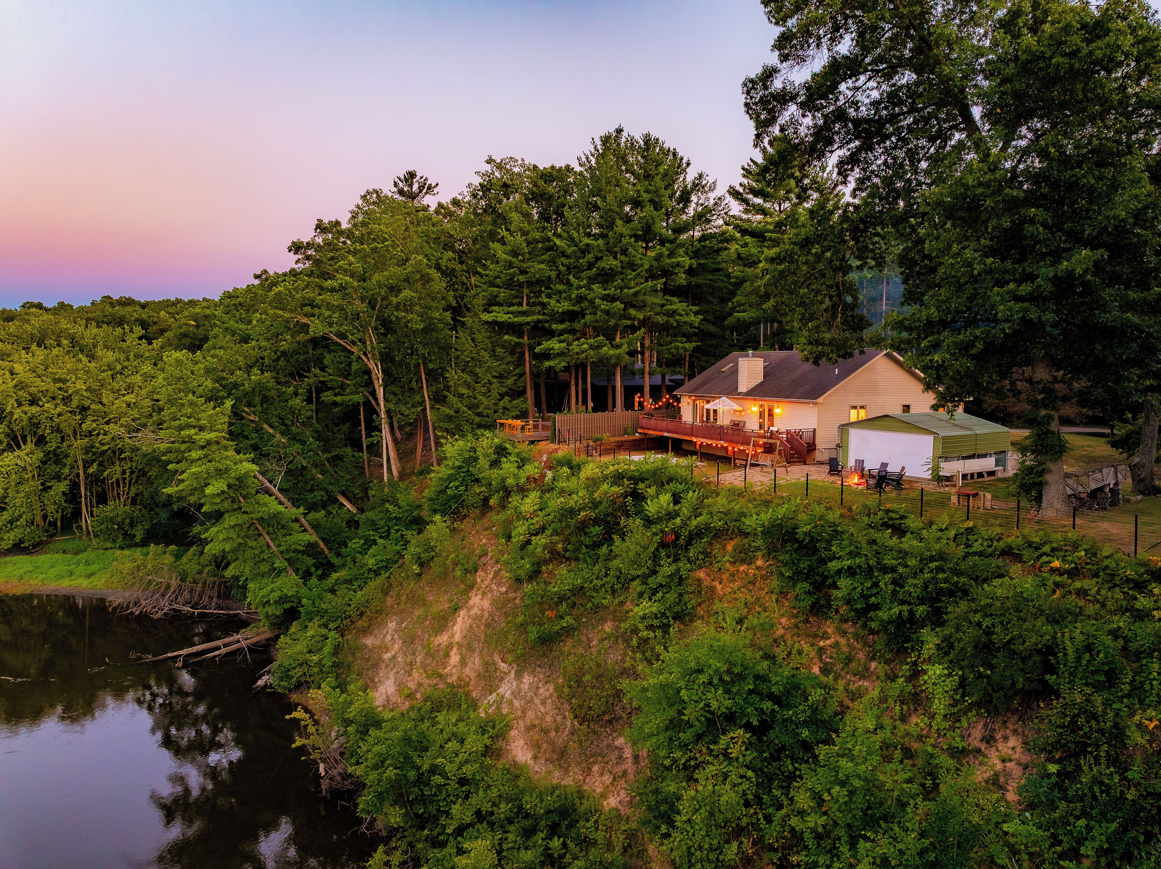 A house with a deck, a covered outdoor area, and a view of a lake surrounded by dense forest.