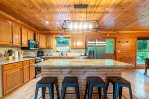 Ein Holzblockhaus-Interieur mit einer großen Kücheninsel, Barhocker und Blick ins Freie.