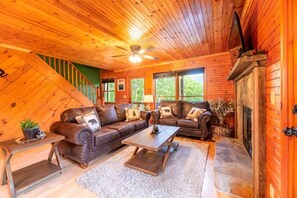 Ein Holzblock-Innenraum mit einer Sofagarnitur, einem Kamin und einem Deckenventilator.