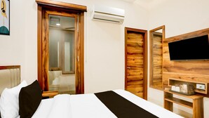 A hotel room with a bed, a television, an air conditioning unit, and wooden decor. - Saver Single MMC Inn (Ludhiana)