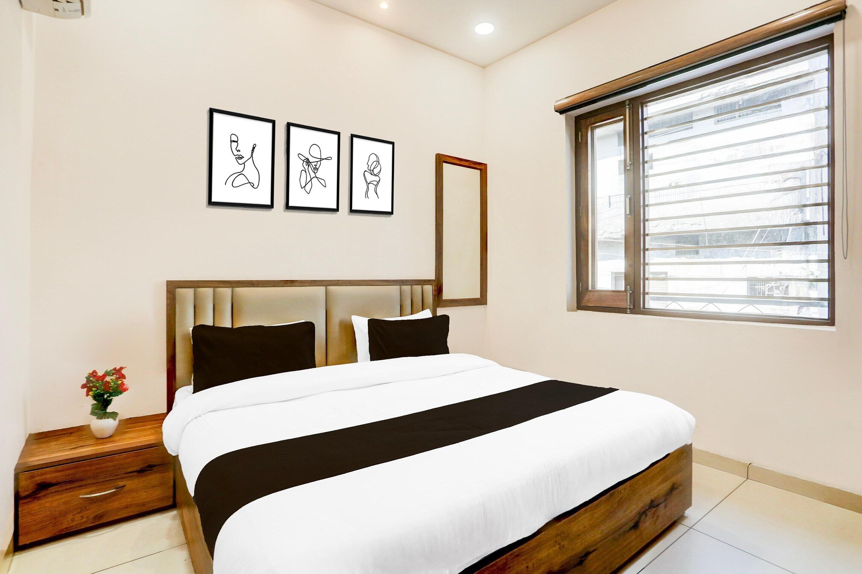 Un dormitorio con una cama, una mesita de noche, un espejo y tres cuadros en la pared.