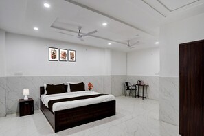 A modern bedroom with a bed, bedside table, nightstand, ceiling fan, and artwork on the wall. - Deluxe Vikas Nagar Post Office Metro (Lucknow)