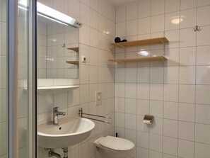 A bathroom with a sink, toilet, mirror, and two wooden shelves. - Ferienwohnung in Orth auf Fehmarn (Fehmarn)
