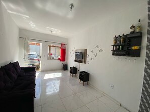 Una sala de estar con un sofá, un televisor, un estante empotrado con botellas y una ventana con cortinas.