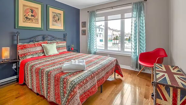 A bedroom with a bed, a red chair, a window with curtains, and two framed posters on the wall. - 2 Bed 2 Bath in Orleans (Ottawa)