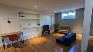 A modern living room with a wooden floor, a red chair, a dark blue sofa, a TV, and a window with blinds. - 2 Bed 2 Bath in Orleans (Ottawa)