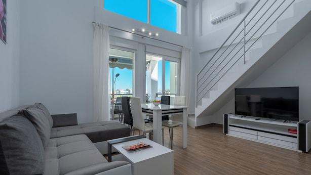 A modern living room with a sofa, coffee table, TV, and a dining area with a table and chairs. - SLV Nefeli Apartment (Pangaio)