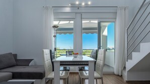 A modern living room with a sofa, dining table, and chairs, a staircase, and a balcony with a view. - SLV Nefeli Apartment (Pangaio)