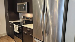 A modern kitchen with dark cabinetry, stainless steel appliances, and a patterned rug.