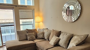 A living room with a sectional sofa, a round mirror, and a lamp.
