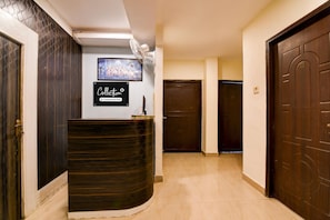 Zona de recepción con un mostrador de madera oscura, un cuadro enmarcado en la pared y una puerta cerrada al fondo.