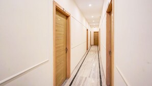A long, narrow hallway with wooden doors on both sides, leading to a room at the end. - Classic With Balcony Surajpur Greater Noida (Greater Noida)