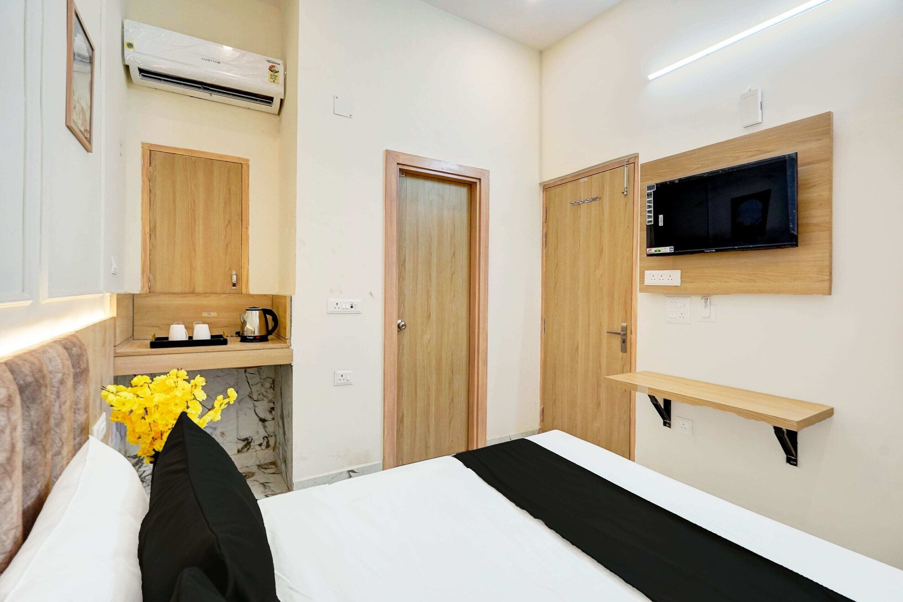 A hotel room with a bed, a TV mounted on the wall, a wooden shelf, and a door.