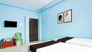 Ein Hotelzimmer mit zwei Betten, einem Fernseher, einem grünen Sessel, einem Schreibtisch mit Wasserkocher und gerahmten Bildern an der Wand.